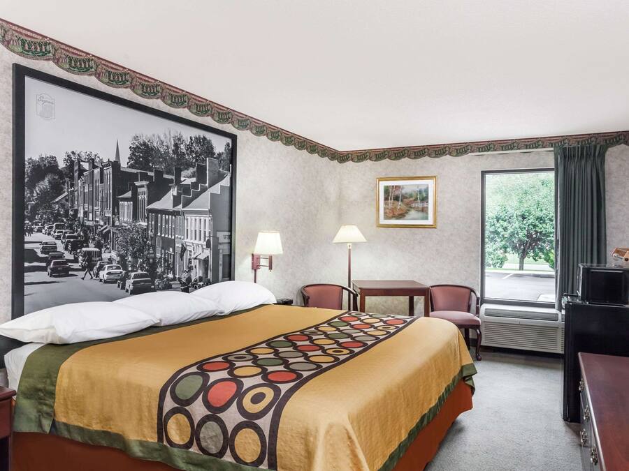 A hotel room with a large bed, a desk, a chair, a TV, and a window with curtains.