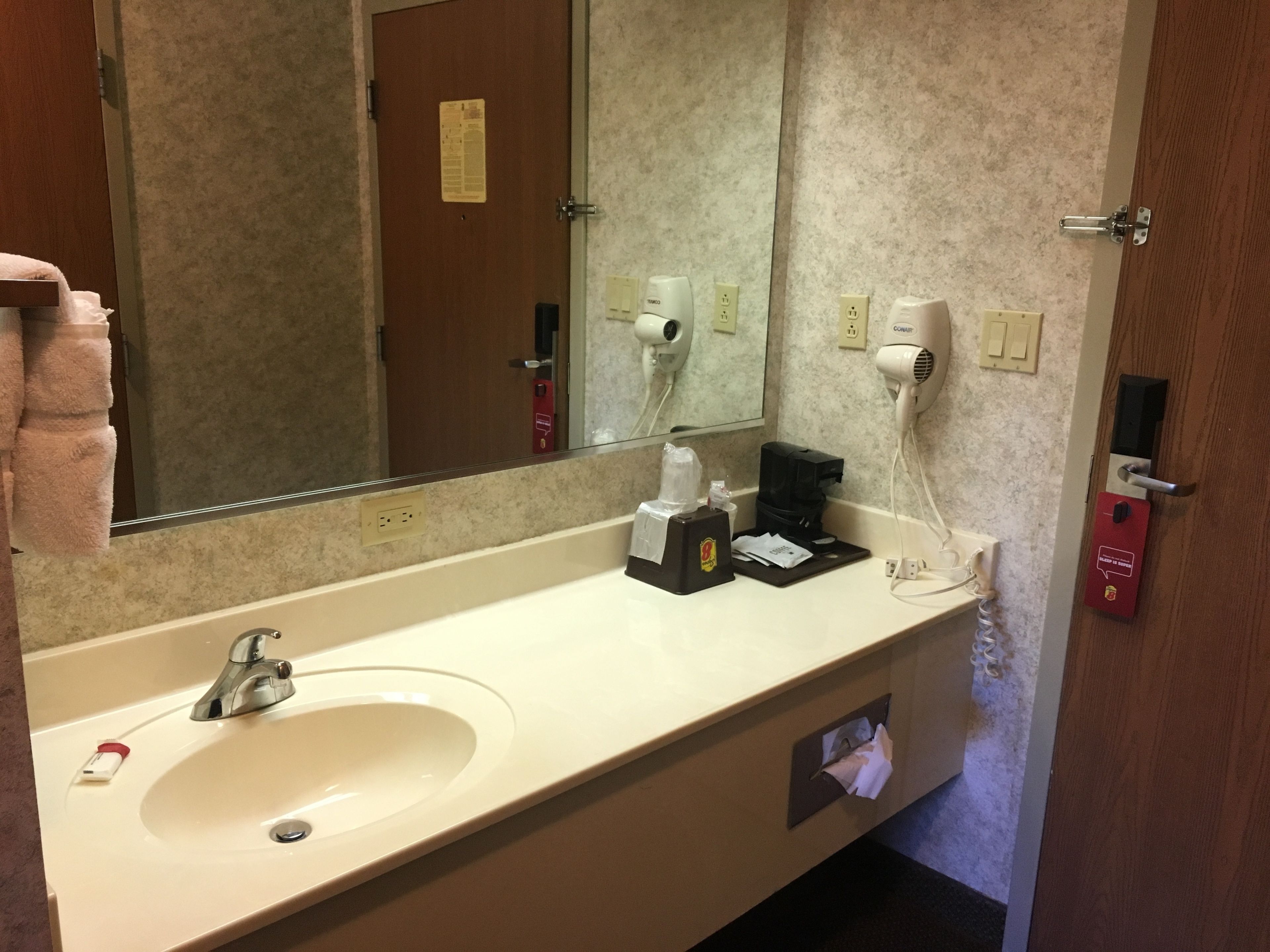 A hotel bathroom with a sink, mirror, towel rack, hairdryer, and a coffee machine.