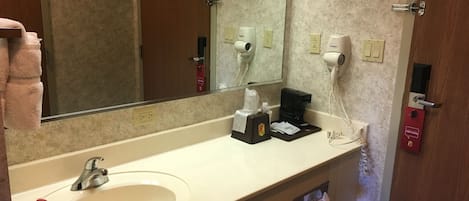 A hotel bathroom with a sink, mirror, towel rack, hairdryer, and a coffee machine.