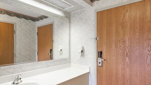 Une salle de bain avec un grand lavabo blanc, des portes en bois et un miroir orné d’un cadre décoratif.