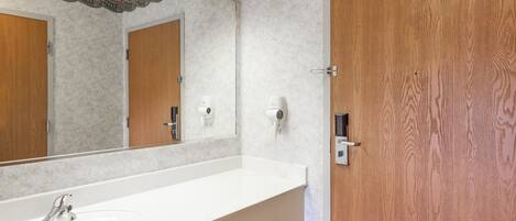 A bathroom with a large white sink, wooden doors, and a mirror with a decorative border.
