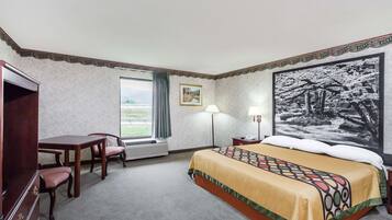 Una habitación de hotel con cama, escritorio, sillas, ventana con cortinas, lámpara y un cuadro en la pared.