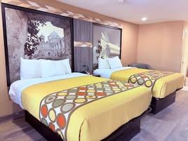 Habitación de hotel con dos camas, cada una con cubrecama amarillo y almohadas blancas. En la pared, un mural muestra un edificio histórico y un avión moderno.