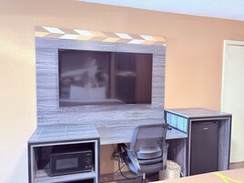 Un espacio de oficina moderno con televisión integrada, un escritorio, una silla y un refrigerador pequeño.