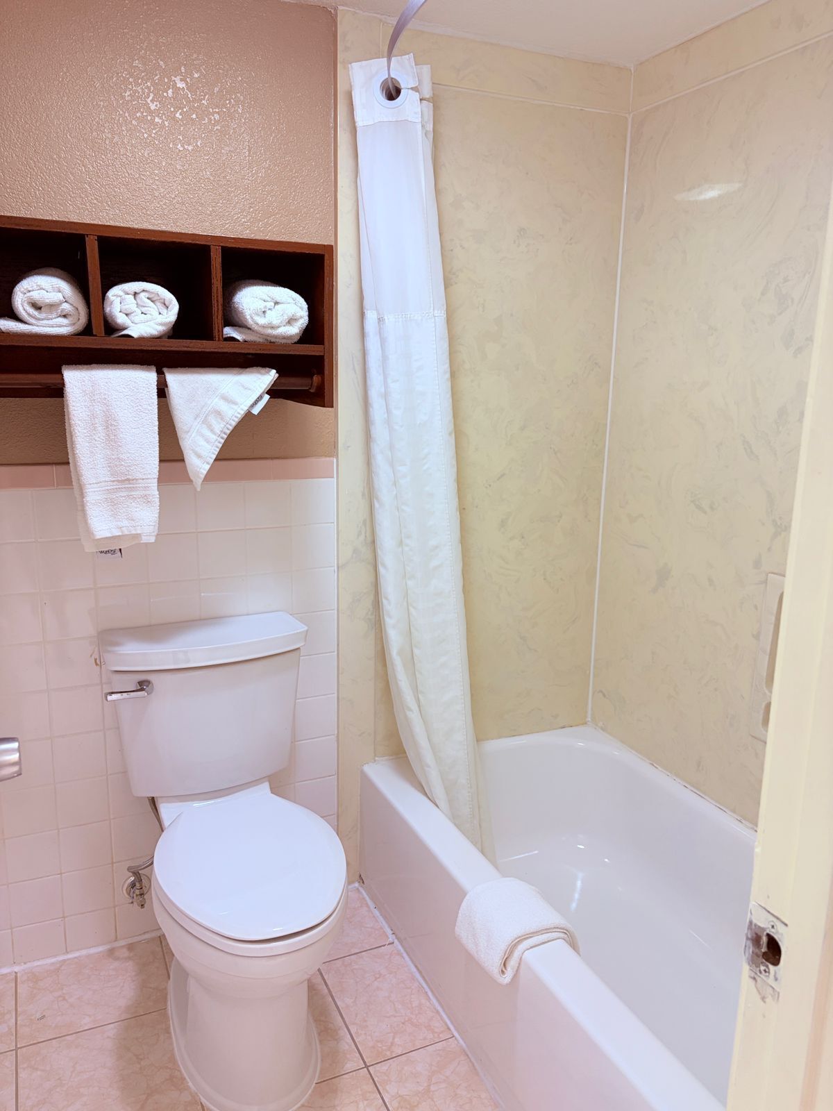 A bathroom with a toilet, a bathtub, and a shower curtain. There are towels hanging on a shelf above the toilet.