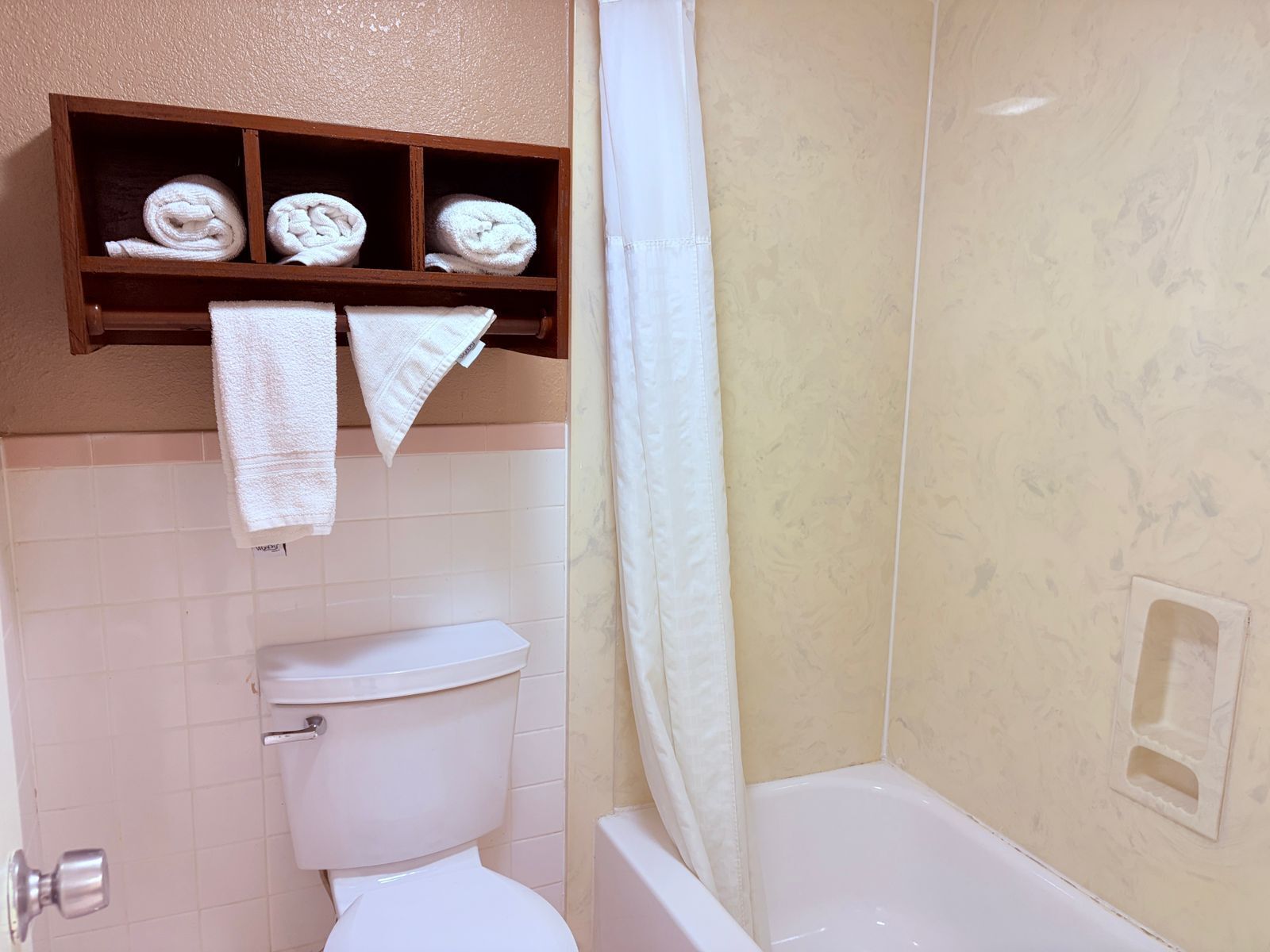 Et badeværelse med toilet, badekar og en hylde med håndklæder.