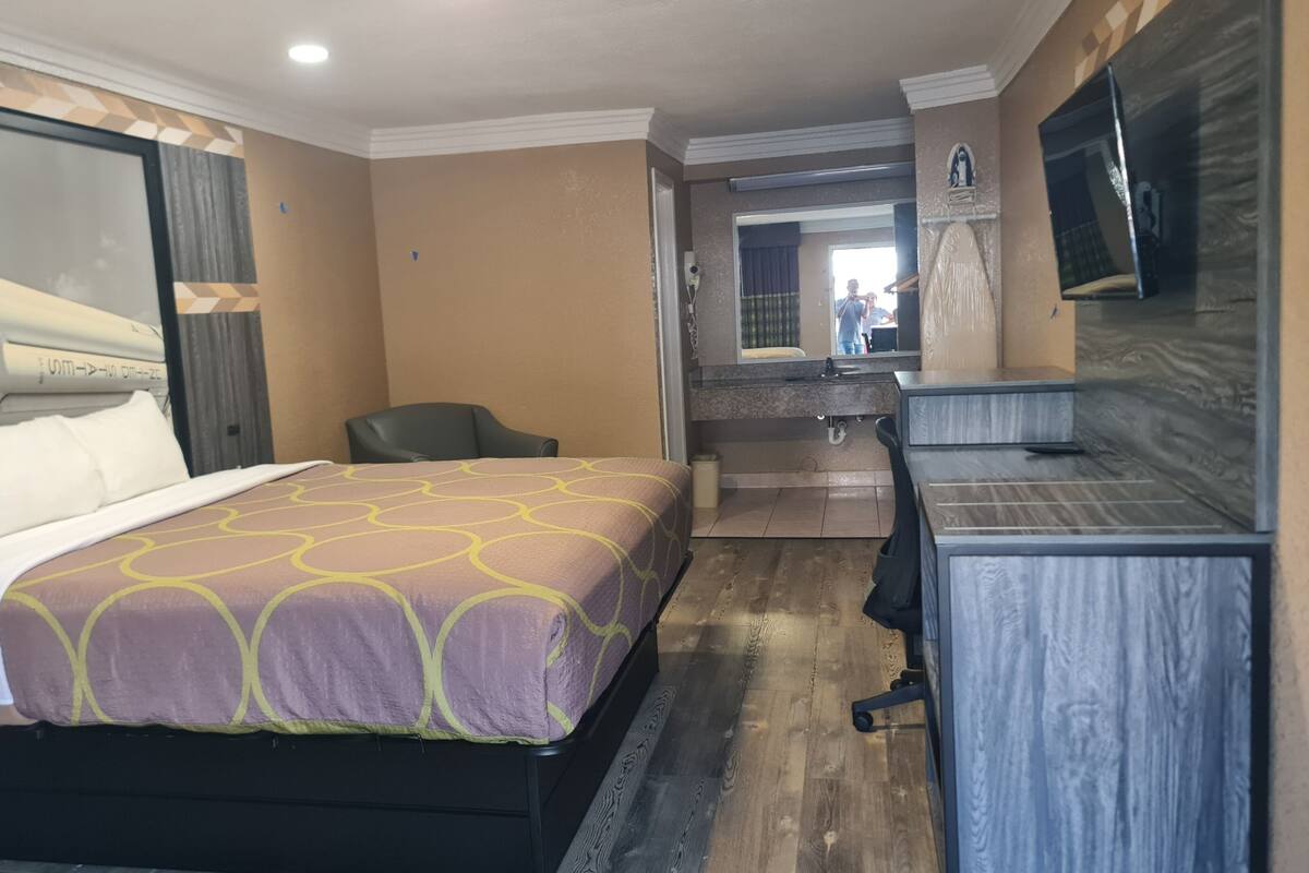 A hotel room with a bed, a desk, a chair, a bathroom, and a large mirror.