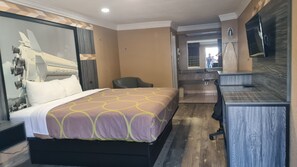 A hotel room with a bed, a desk, a chair, a bathroom, and a large mirror.