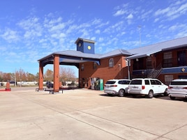Una estación de servicio con toldo azul, edificio de ladrillo y varios SUVs blancos estacionados.