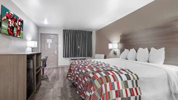 A hotel room with a bed, a desk, a chair, a television, and a window with curtains.