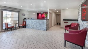Un área de recepción con piso de diseño espiga, un mostrador de recepción con pared de acento roja y sillones tapizados en rojo.