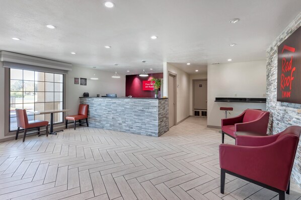 Un área de recepción con piso de diseño espiga, un mostrador de recepción con pared de acento roja y sillones tapizados en rojo.
