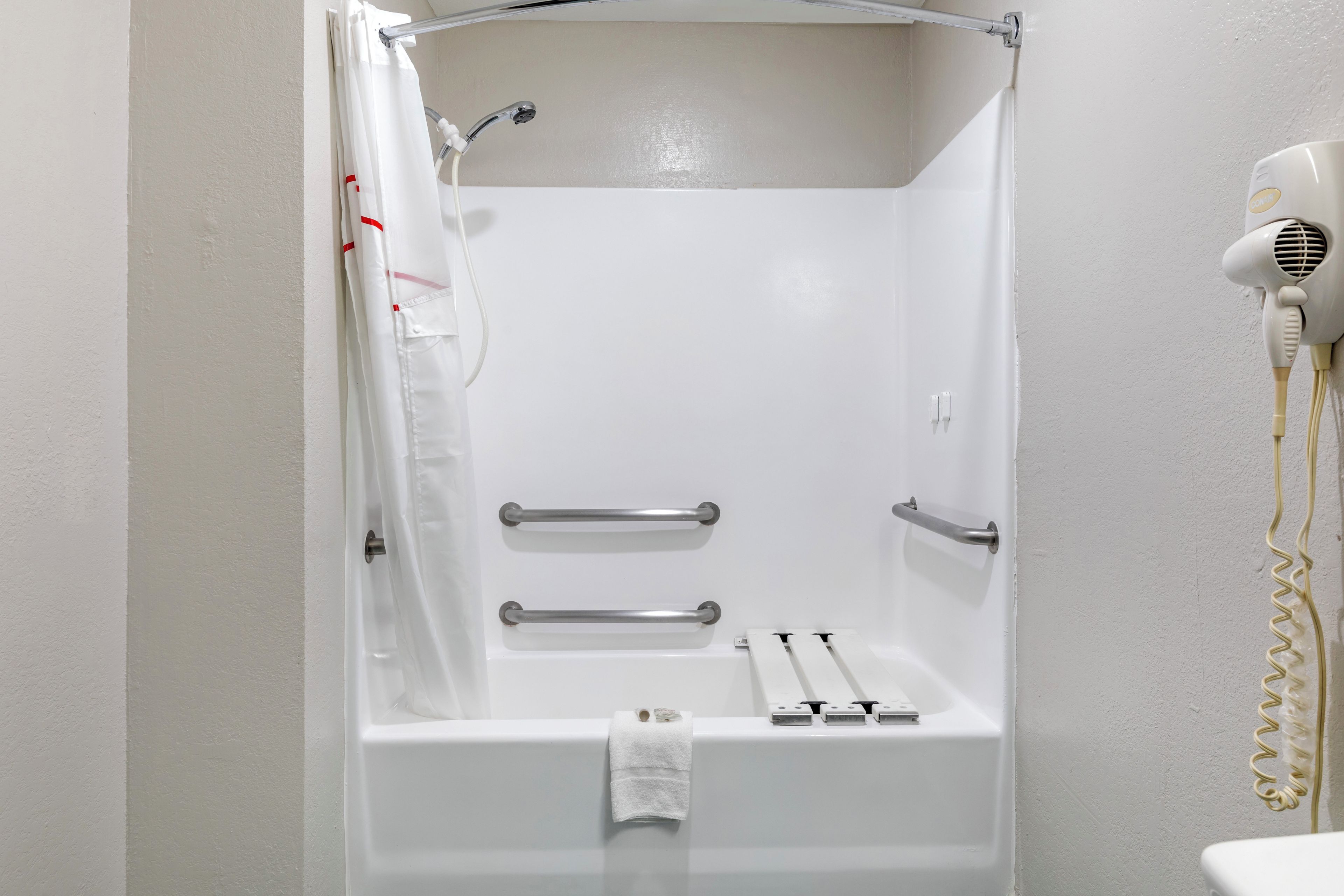 A white shower stall with a handheld showerhead, a towel rack, and a hairdryer on the wall.