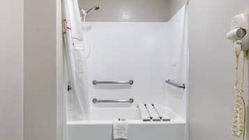 A white shower stall with a handheld showerhead, a towel rack, and a hairdryer on the wall.