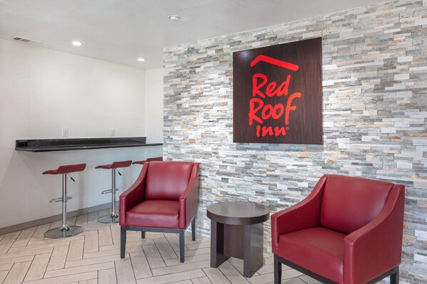 A Red Roof Inn reception area with a stone wall, two red leather chairs, a small round table, and a bar counter. - Red Roof Inn Canton, TX (Canton)