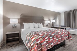 Habitación de hotel con una cama grande, dos mesitas de noche con lámparas, un escritorio y una ventana con cortinas.