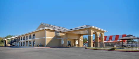 A hotel with a covered outdoor area, a parking lot, and a building with a red roof.