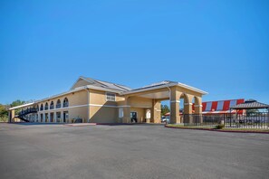 A hotel with a covered outdoor area, a parking lot, and a building with a red roof. - Red Roof Inn Canton, TX (Canton)