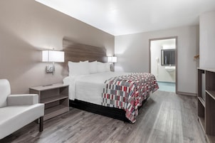Una habitación de hotel con cama, mesitas de noche, una silla, armario y un baño visible a través de una puerta abierta.