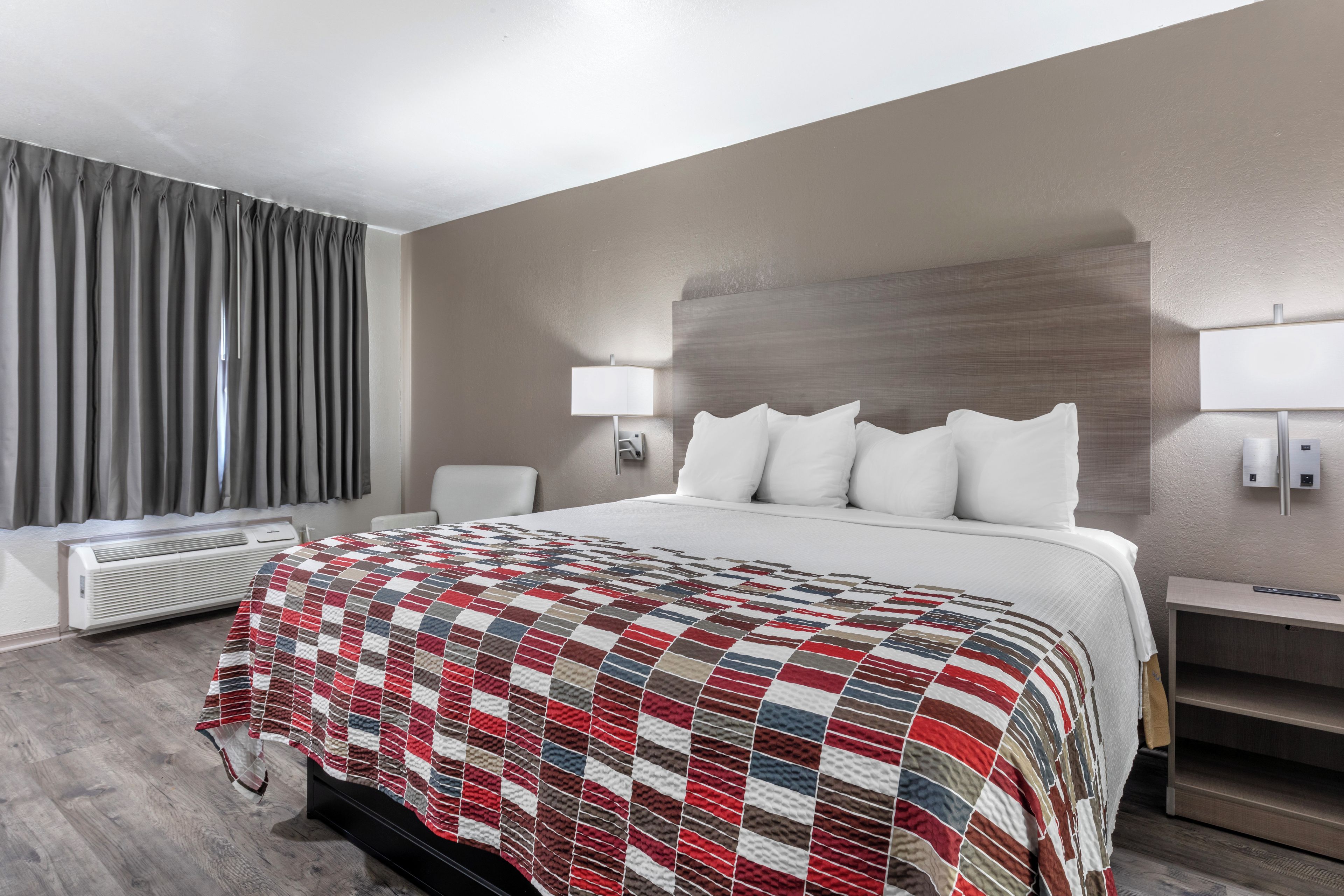 Une chambre d’hôtel avec un lit, une table de chevet, une lampe, un radiateur et une fenêtre avec des rideaux.