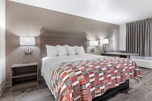 Una habitación de hotel con cama, lámparas de noche, escritorio y ventana con cortinas.