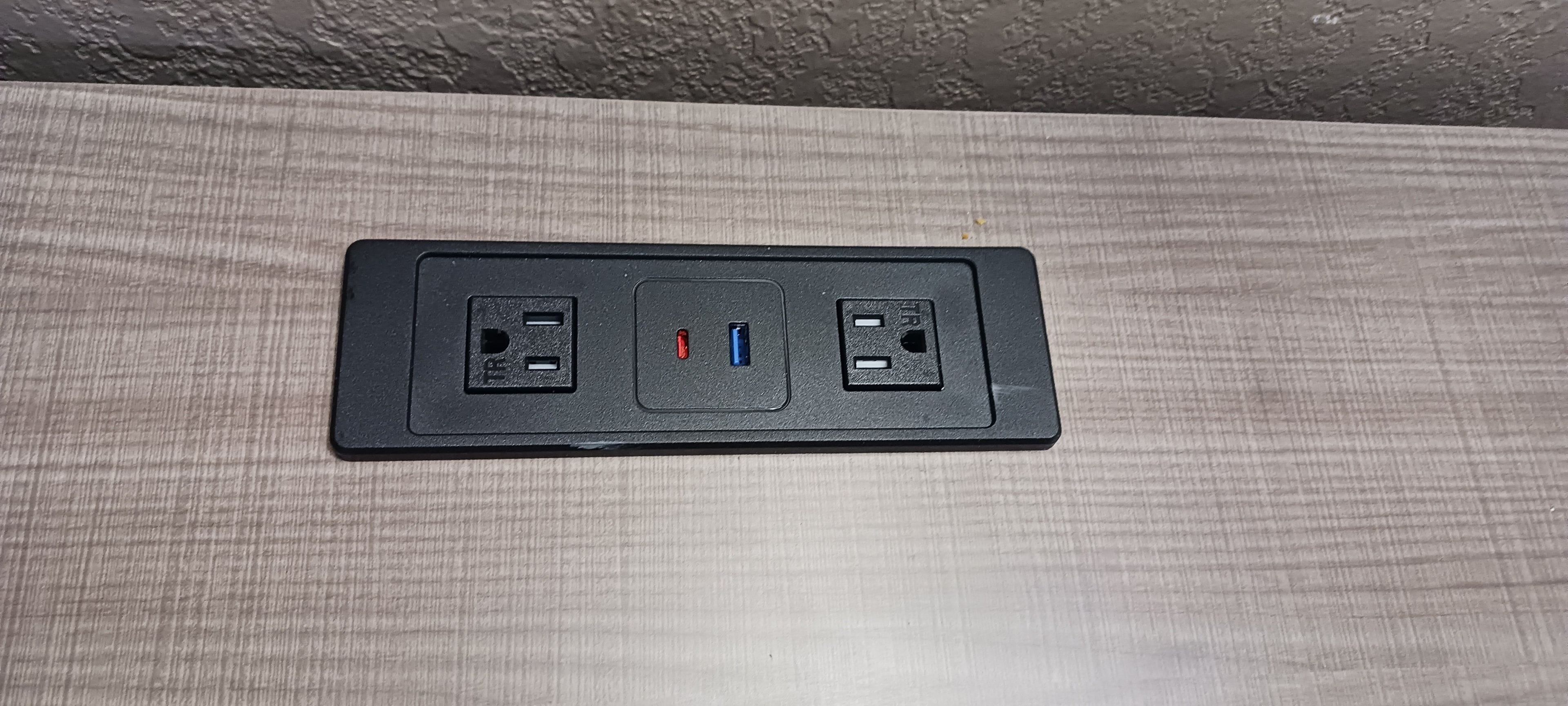 A black power strip with two USB ports and two standard electrical outlets on a textured wooden surface.