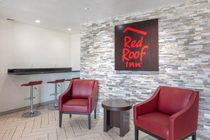 Zona de recepción de Red Roof Inn, con pared de piedra, dos sillas rojas, una mesita y una barra.