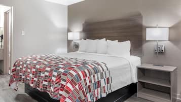 Habitación de hotel con cama, mesita de noche, lámpara y aplique de pared.