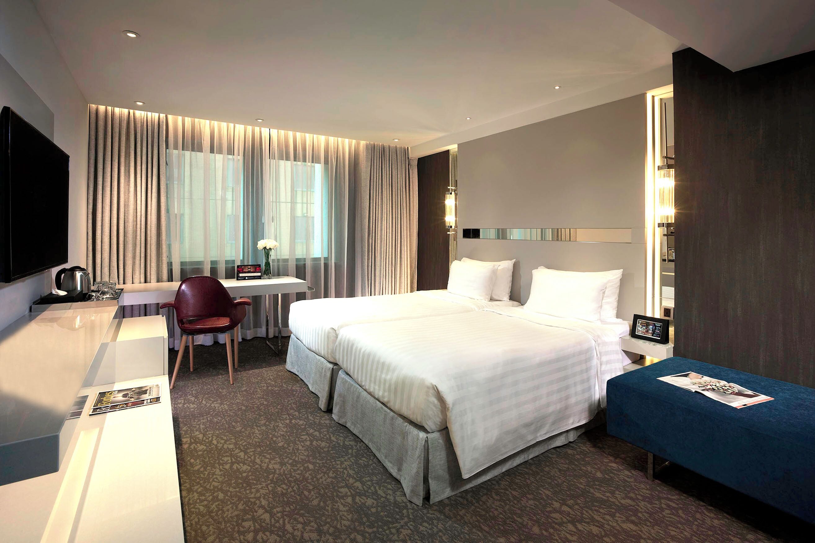 A hotel room with a large bed, a desk with a chair, a TV, and a small table with a lamp.