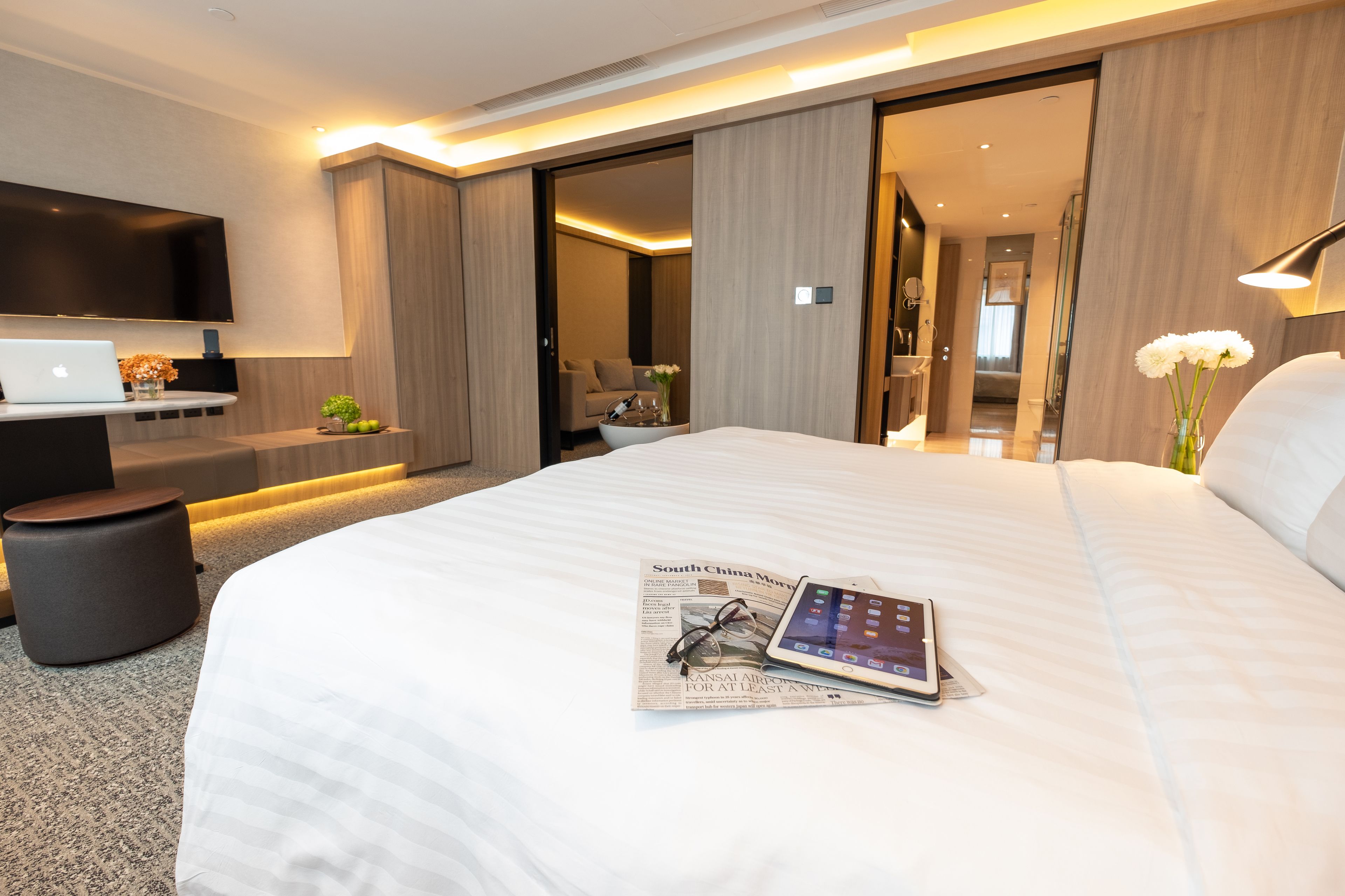 Une chambre d’hôtel moderne avec un grand lit, un téléviseur à écran plat, un ordinateur portable et une tablette posés sur le lit.