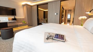 Habitación de hotel moderna con una cama grande, un televisor de pantalla plana, una laptop y una tablet sobre la cama.