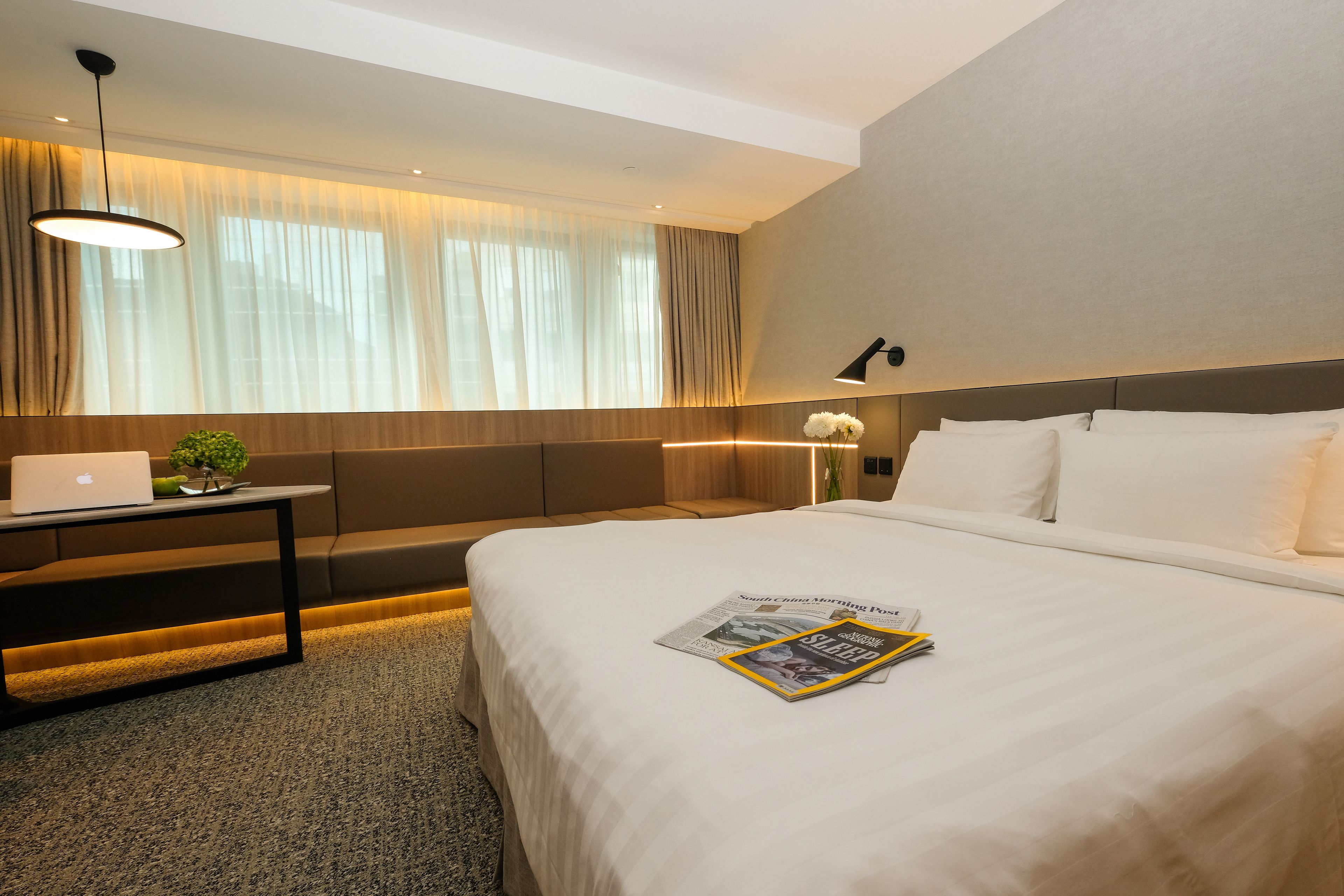 A hotel room with a large bed, a desk with a laptop, a sofa, and a window with curtains.