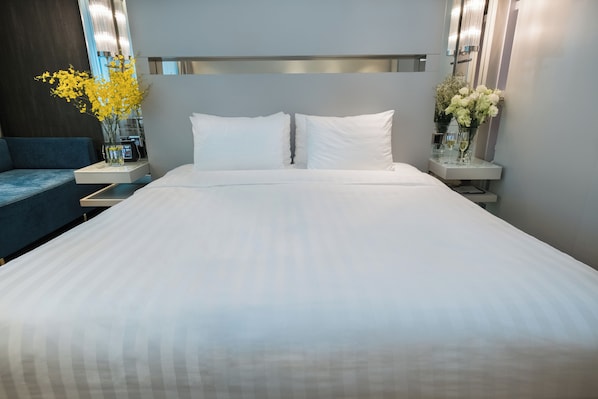 A neatly made bed with white linens, two bedside tables with vases of flowers, and a modern headboard. - Nathan Hotel (Kowloon)