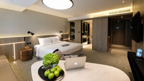 A modern hotel room with a bed, bedside table with a laptop, a bowl of apples, and a vase of flowers. - Nathan Hotel (Kowloon)