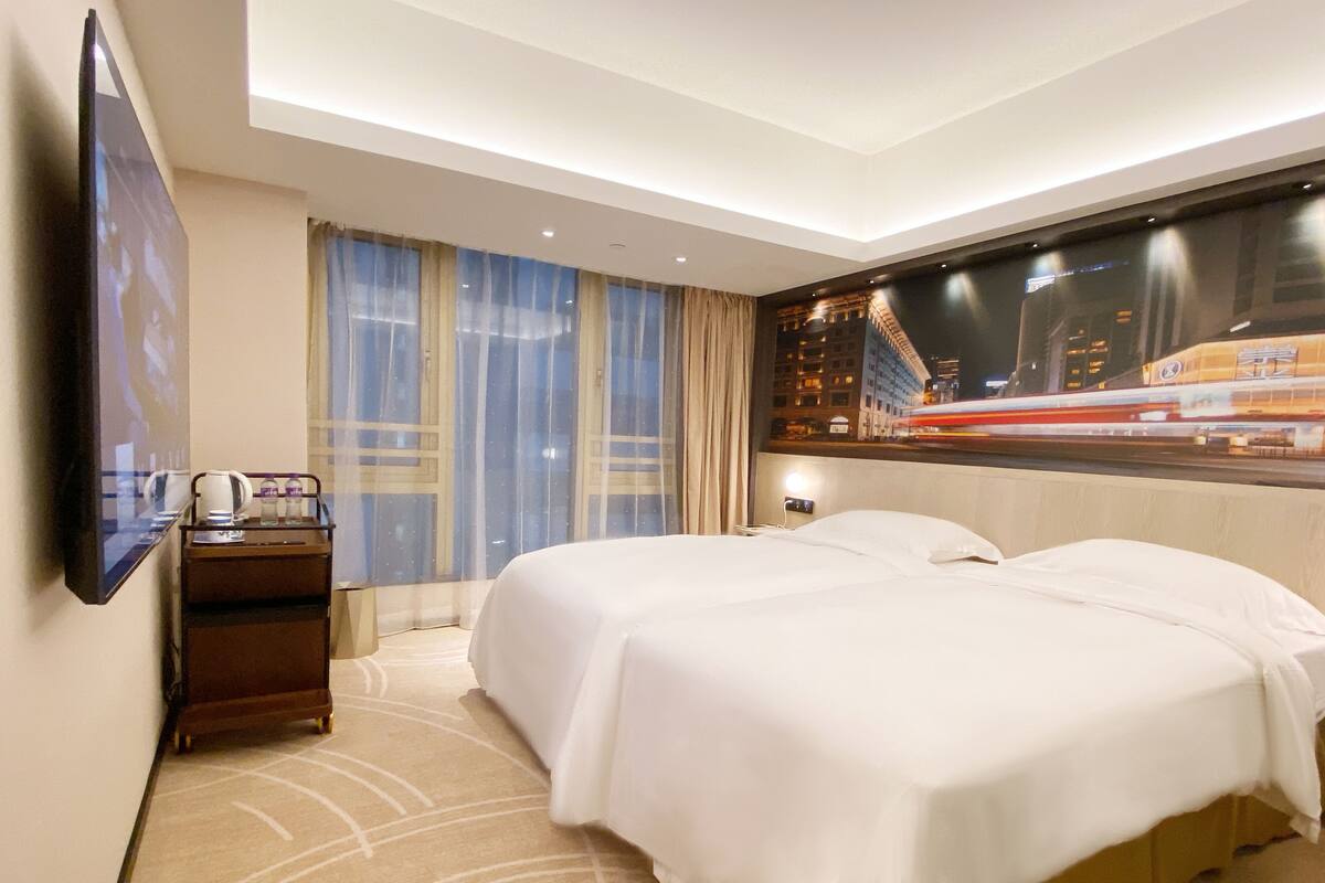 A hotel room with a large bed, a TV mounted on the wall, a nightstand, and a window with curtains.