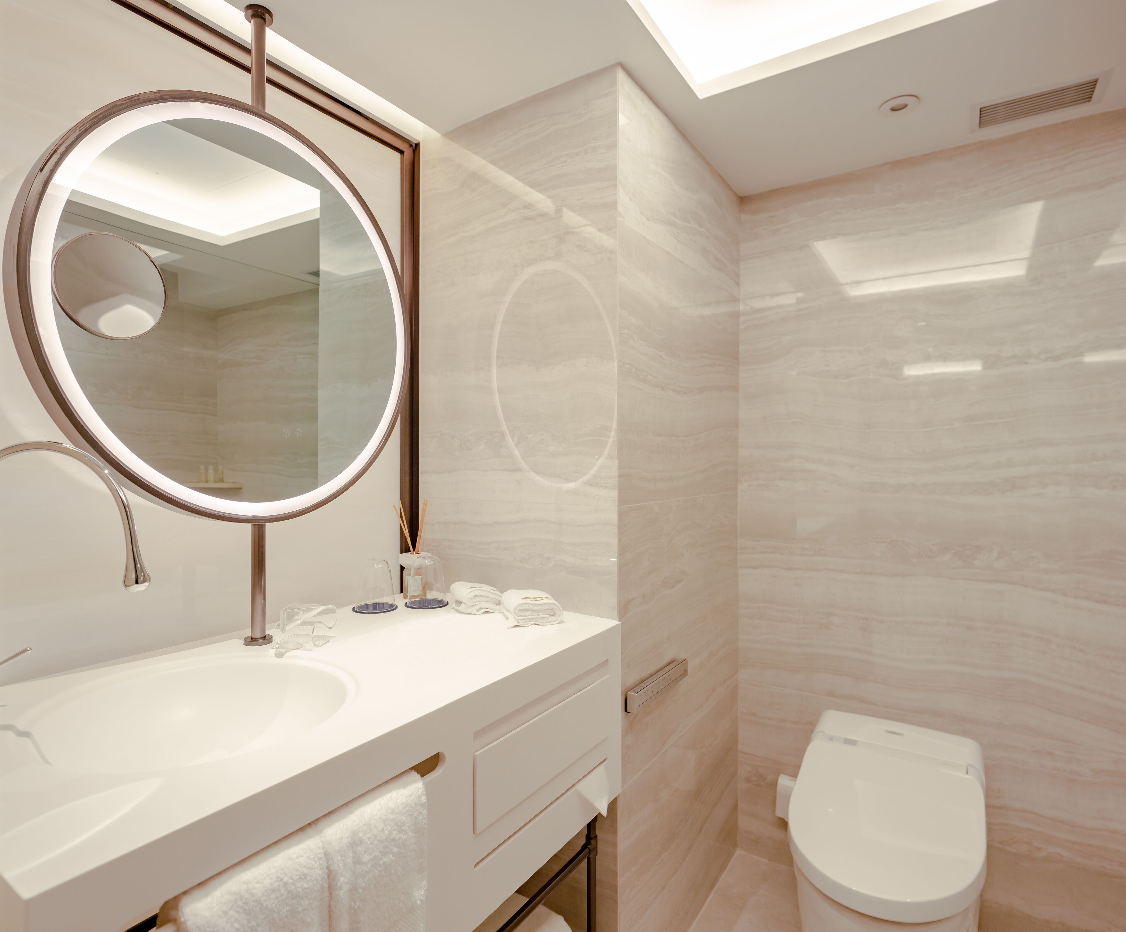 A modern bathroom with a round mirror, a sink, a toilet, and a skylight.