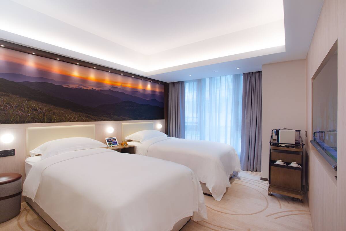 A hotel room with two beds, a nightstand, a TV, and a large window with curtains.