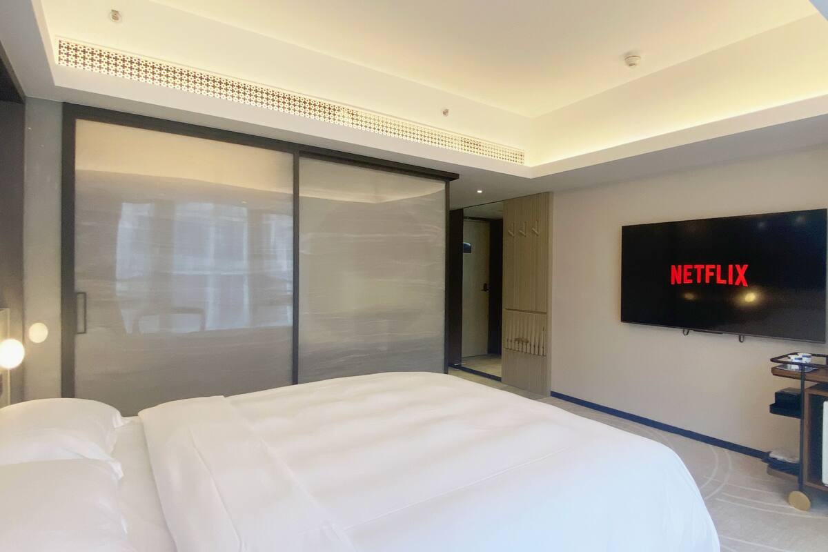 A hotel room with a large bed, a sliding door closet, a flat-screen TV on the wall, and a desk with a water bottle.