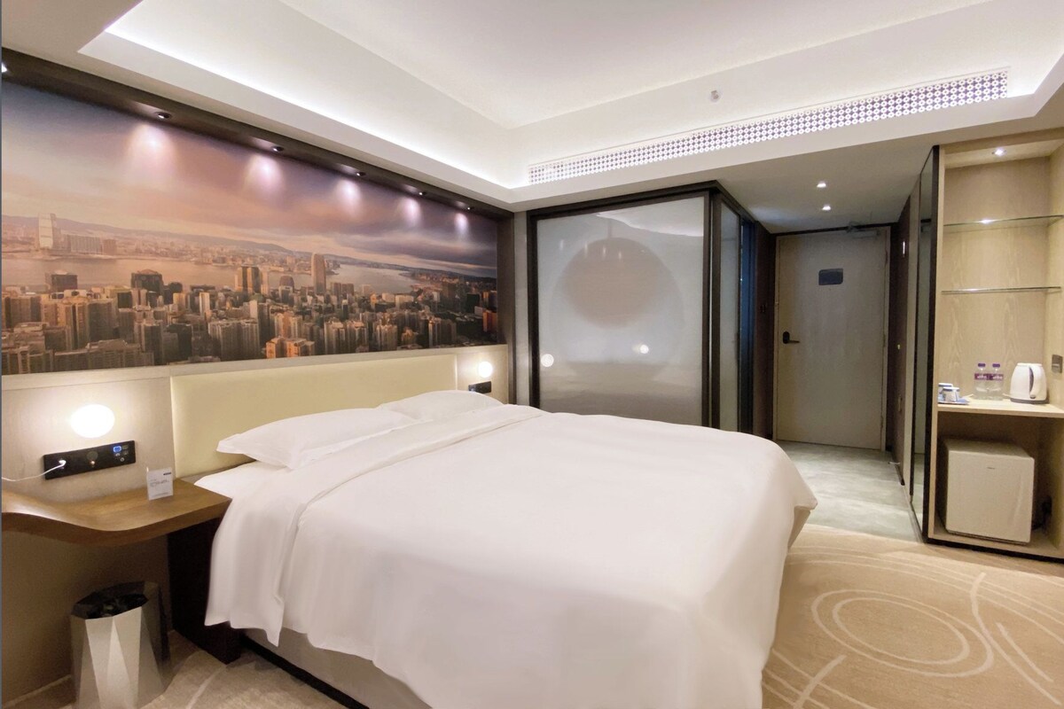 A hotel room with a bed, a nightstand, a wall-mounted TV, and a bathroom door.