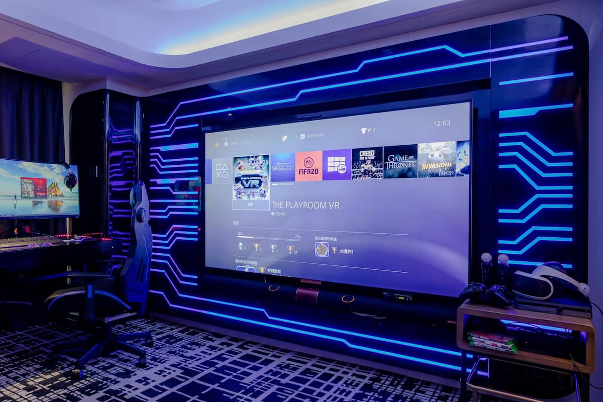 A gaming room with a large screen displaying games, a gaming PC, and a VR headset.