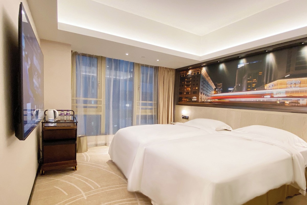 A hotel room with a bed, a nightstand, a TV, and a window with curtains.