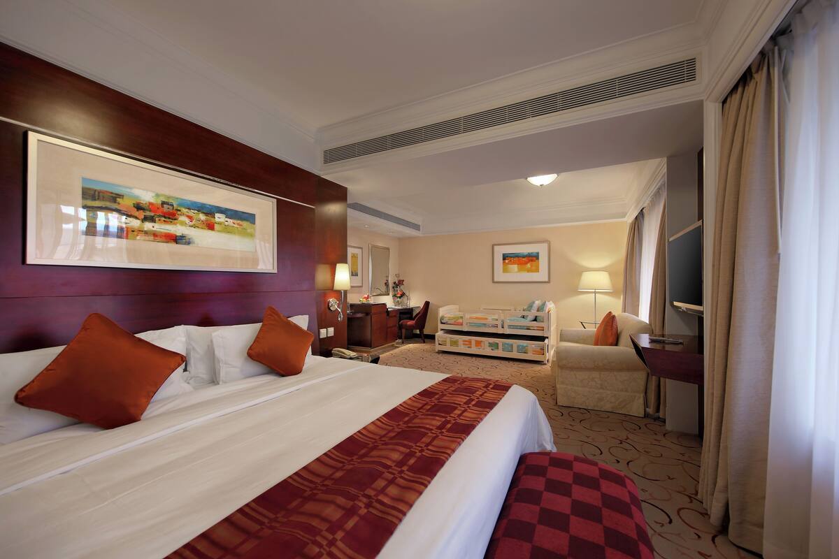 A hotel room with a large bed, a desk, a chair, a sofa, and a TV.