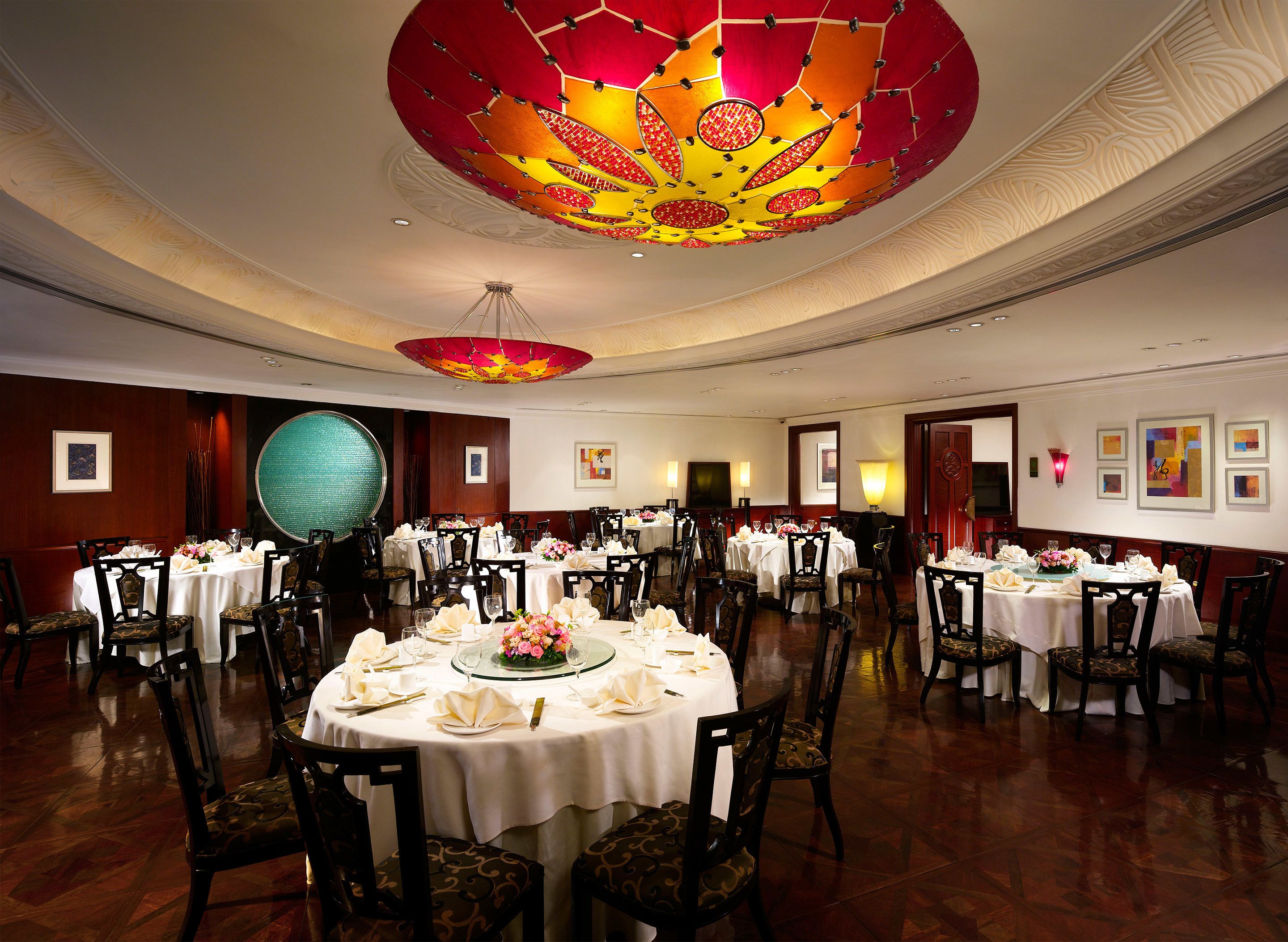 Un salón de banquetes con mesas redondas, sillas y una lámpara decorativa grande en el techo.