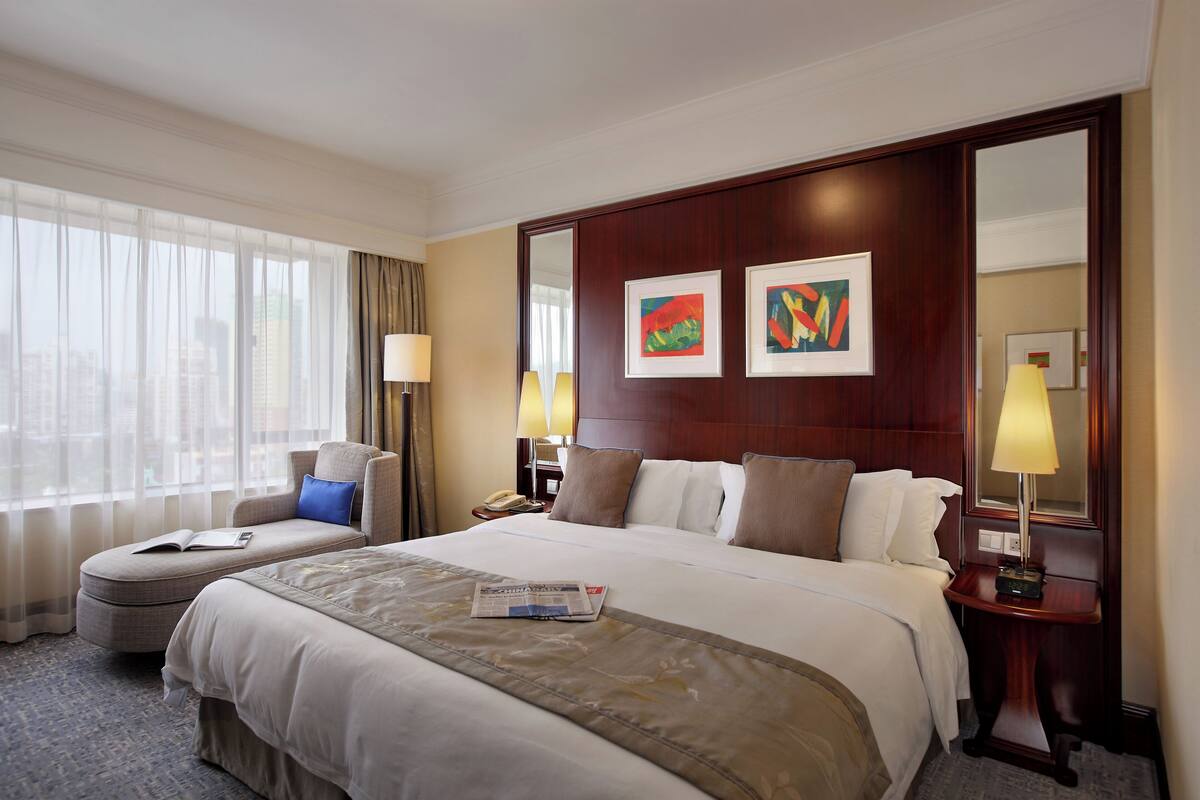 A hotel room with a large bed, a sofa, a desk, and a window with curtains.