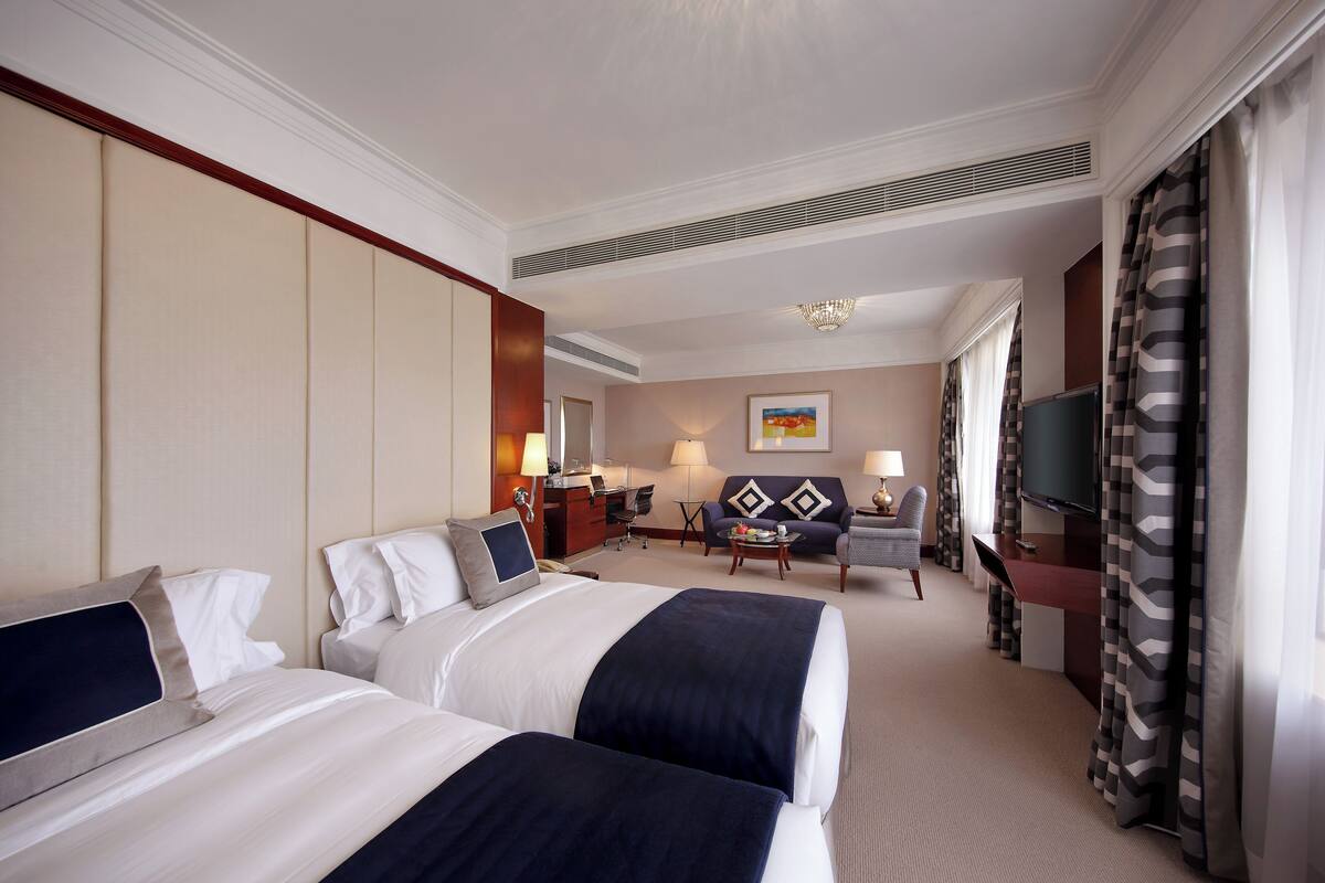 A hotel room with two beds, a desk, a chair, a TV, and a painting on the wall.