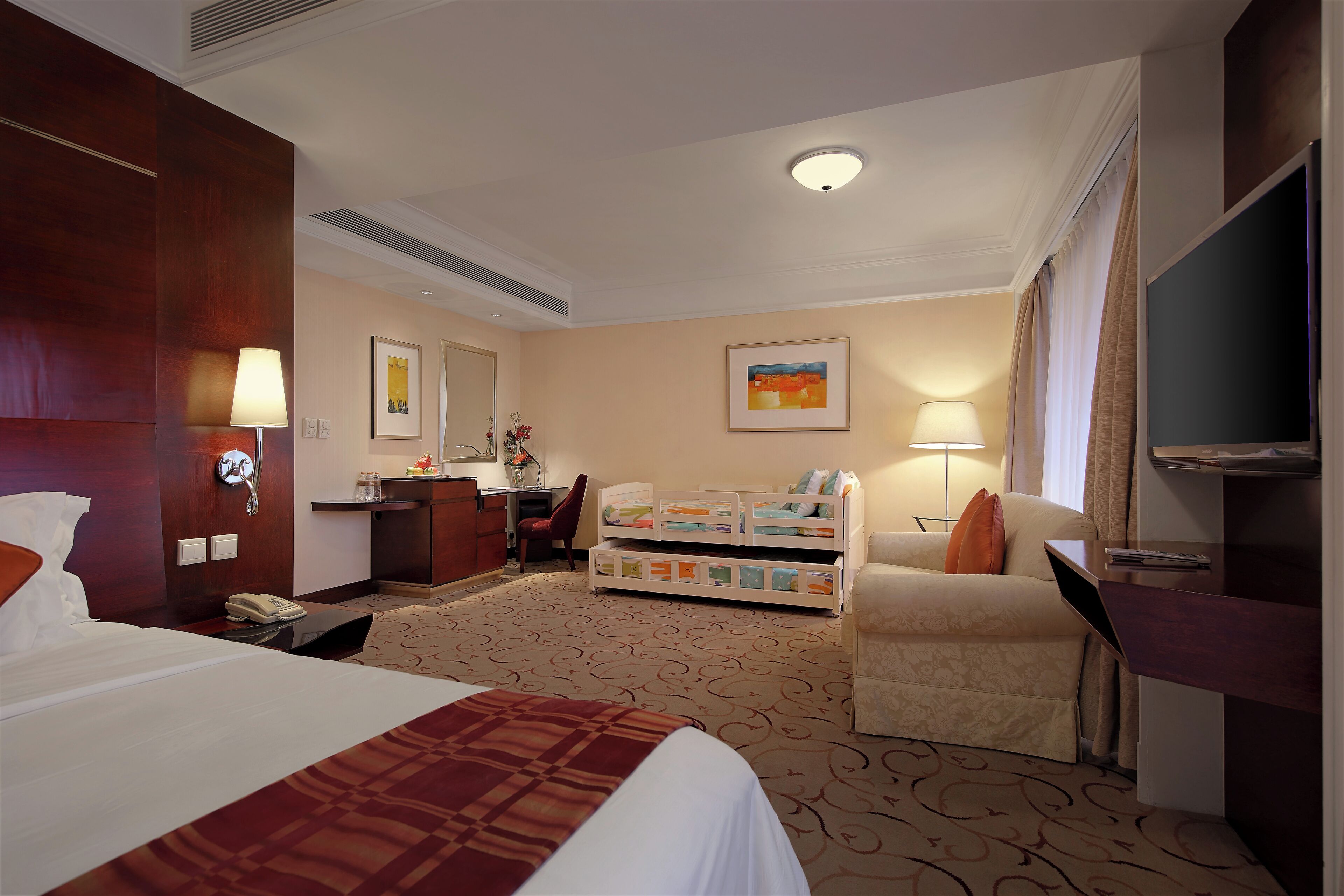 Habitación de hotel con cama, escritorio, silla, televisor y una pequeña kitchenette.
