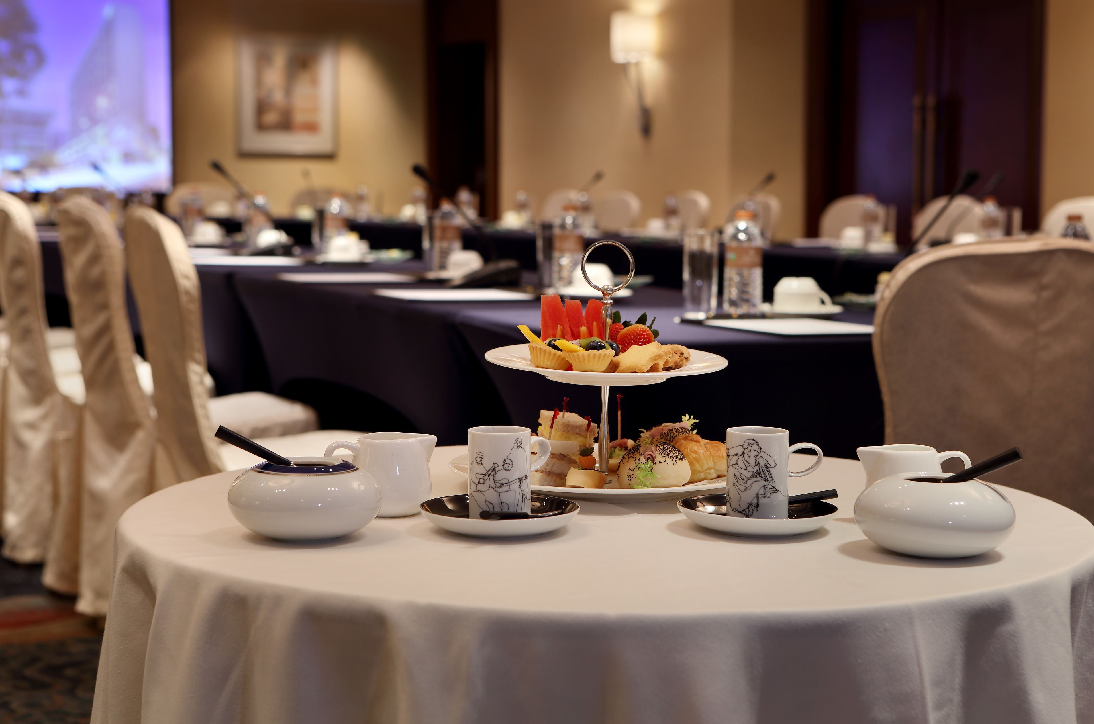 A conference room with round tables, white tablecloths, and a tiered dessert stand.