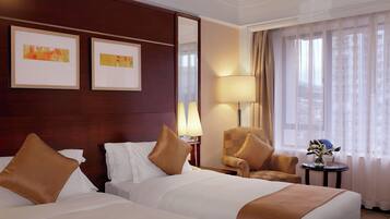 A hotel room with two beds, a sitting area with a chair, a lamp, and a small table with a vase of flowers.