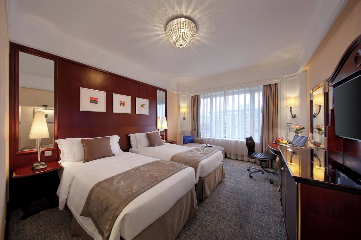A hotel room with two beds, a desk with a computer, a TV, and a large mirror.