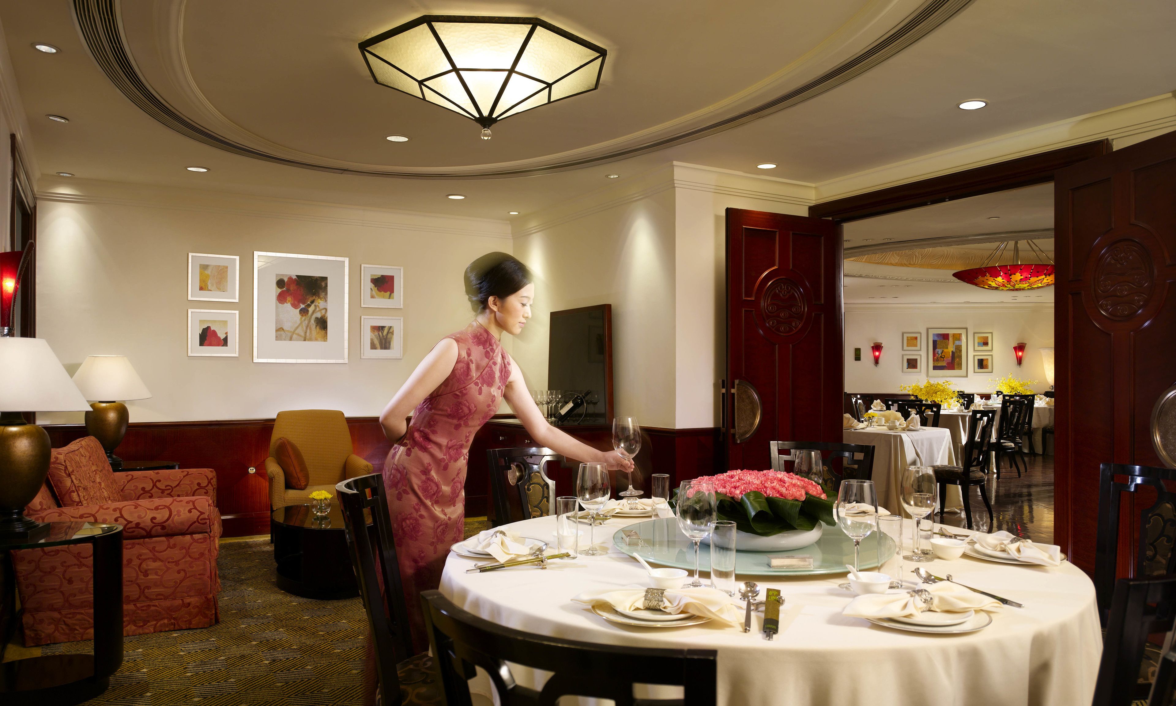 A well-lit dining area with a round table set for a meal, a red door, and a chandelier.